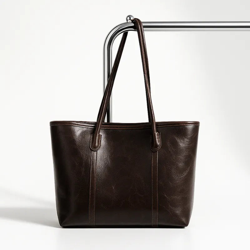 Bolsa tote marrom escuro em vista frontal. A foto exibe o acessório em um expositor, destacando a estrutura da bolsa.