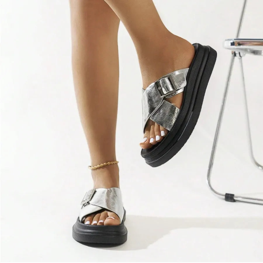 Modelo usando a papete feminina prata de fivela da Rozze, sentada. A imagem mostra o calçado em uso, complementando um look casual e realçando o conforto e a versatilidade.