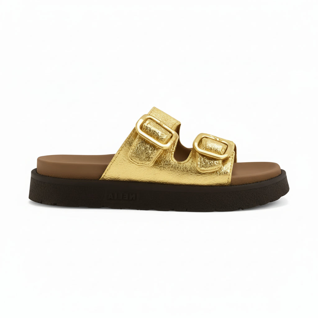 Sandália feminina dourada com fivelas, vista lateral em estúdio. A foto destaca o design flatform, o solado preto e as duas fivelas ajustáveis na parte superior.