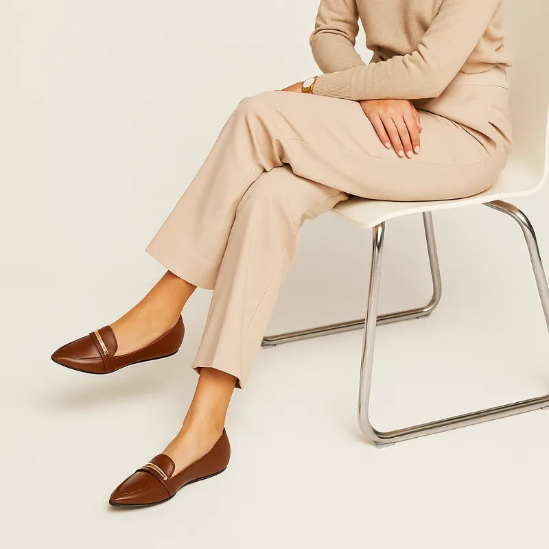 Modelo usando a sapatilha bico fino Valentina Gold da Rozze, sentada. A imagem mostra o calçado em uso, complementando um look casual e confortável com calça bege.