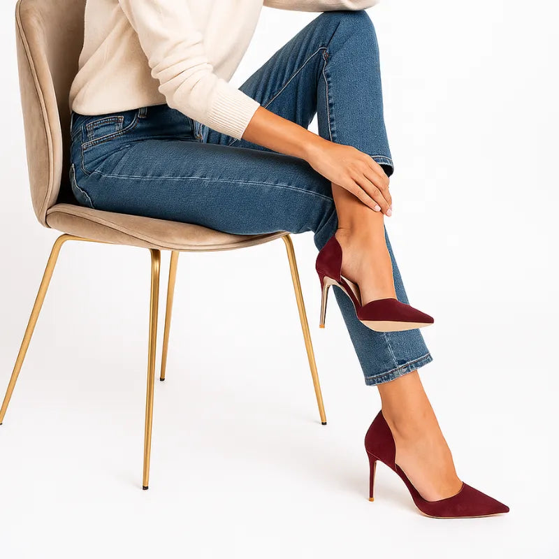 Modelo usando o scarpin vinho de salto agulha, sentada. A imagem mostra o calçado em uso, complementando um look casual com calça jeans e realçando a sua sofisticação.