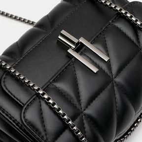 Detalhe do fecho da bolsa acolchoada preta. A foto aproxima o ferrolho prático e a textura matelassê do material, mostrando a qualidade do acabamento.