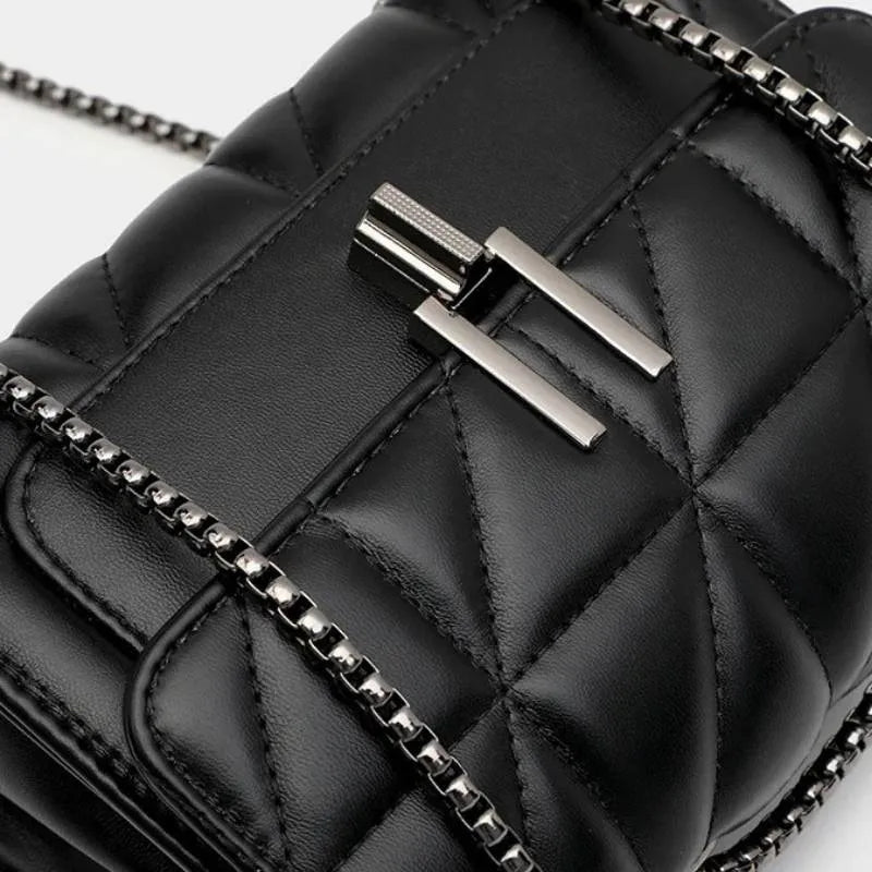 Detalhe do fecho da bolsa acolchoada preta. A foto aproxima o ferrolho prático e a textura matelassê do material, mostrando a qualidade do acabamento.