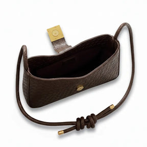 Detalhe do interior da bolsa baguete marrom e da alça ajustável. A imagem foca na funcionalidade e no acabamento.