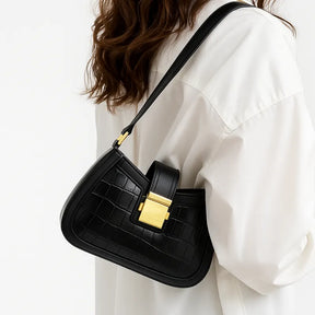 Modelo usando a bolsa baguete preta croco. A imagem em close realça a textura croco e o fecho metálico dourado.