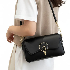 Modelo usando a bolsa baguete preta como crossbody. A imagem realça o fecho redondo dourado e a alça de corrente.