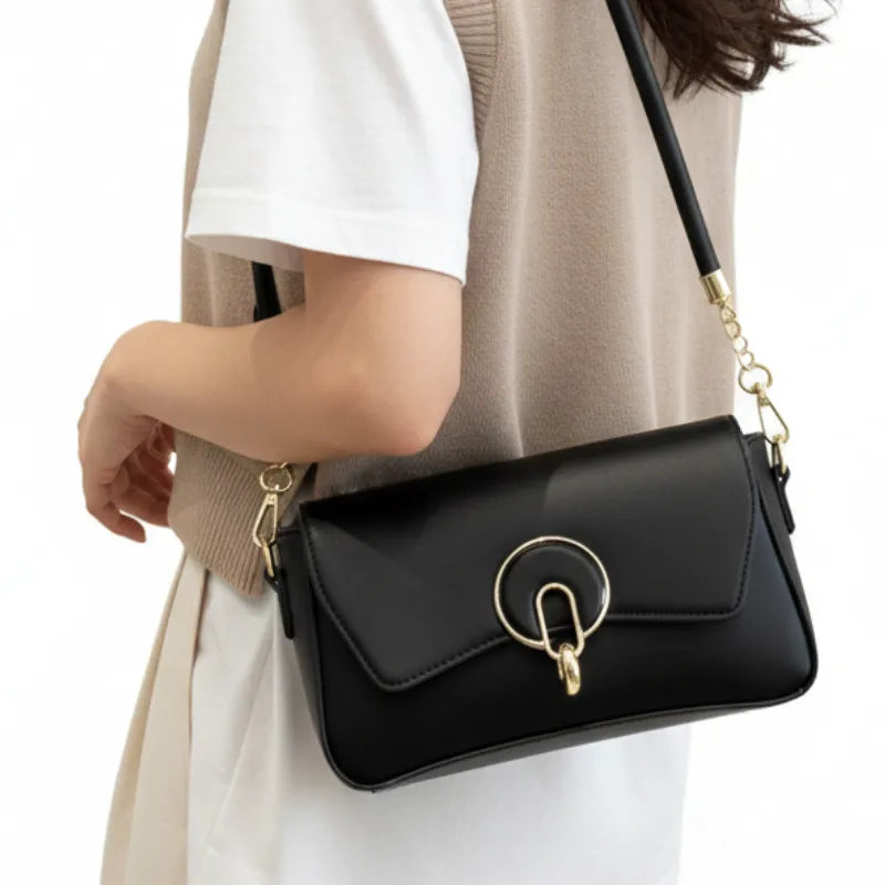 Modelo usando a bolsa baguete preta como crossbody. A imagem realça o fecho redondo dourado e a alça de corrente.