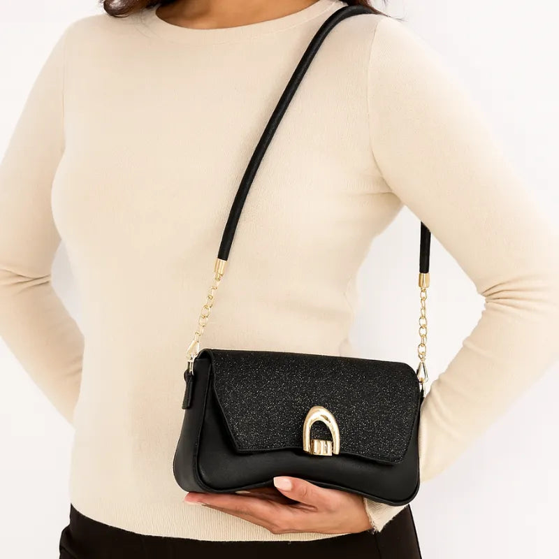 Modelo usando a bolsa baguete preta no ombro. A imagem realça o estilo de festa e o brilho do acessório em um look noturno.
