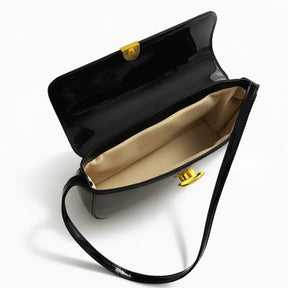 Modelo usando a bolsa baguete preta no ombro. A imagem realça o estilo elegante e o brilho do material em um look noturno.