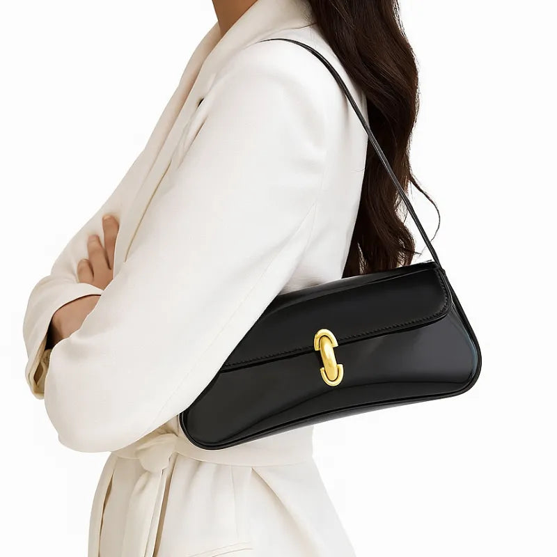 Bolsa baguete preta verniz em vista lateral. A foto exibe a forma do acessório e a alça de ombro curta e sofisticada.