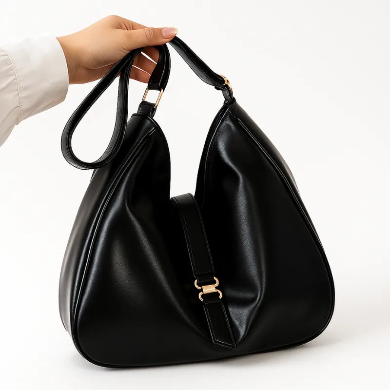 Modelo segurando a bolsa hobo preta pela alça. A imagem mostra o acessório sendo carregado, realçando o tamanho grande e o estilo elegante.