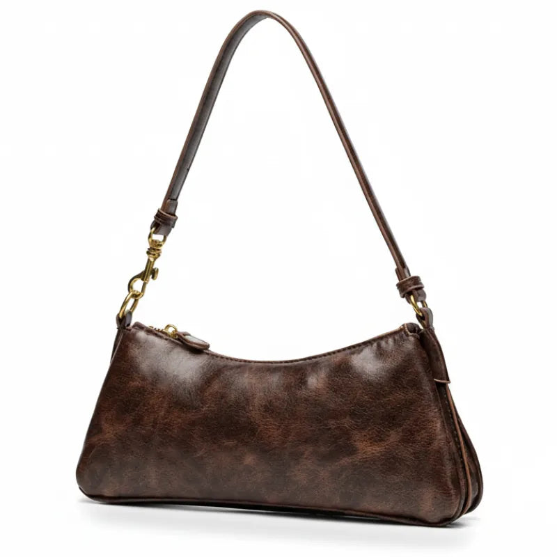 Bolsa baguete marrom em vista de ângulo. A foto exibe o design clássico e os metais com acabamento envelhecido.