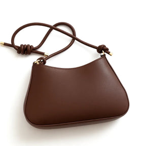 Vista lateral da bolsa de ombro marrom. A foto exibe a forma do acessório e o detalhe de nó na alça.