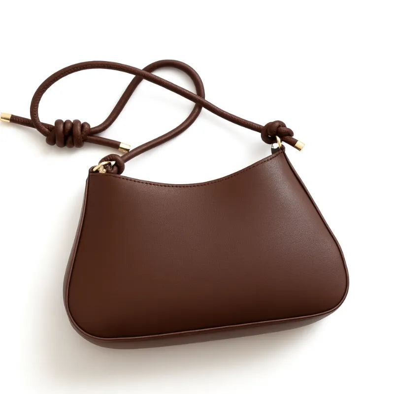 Vista lateral da bolsa de ombro marrom. A foto exibe a forma do acessório e o detalhe de nó na alça.