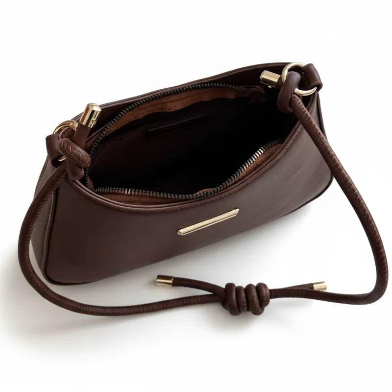 Vista superior da bolsa de ombro marrom aberta. A foto revela o interior e o pequeno detalhe metálico na frente, mostrando a funcionalidade.