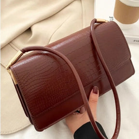 Modelo usando a bolsa de ombro marrom Baguette Croc da Rozze. A imagem mostra o acessório com a alça longa, destacando a versatilidade.