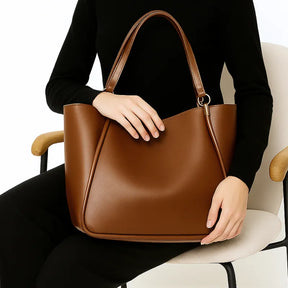 Modelo segurando a bolsa de ombro marrom. A foto realça o Design Curvado sofisticado e os detalhes cravados na costura.