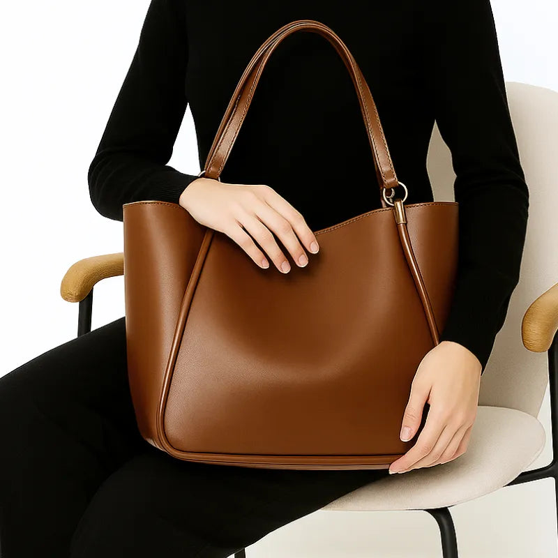 Modelo segurando a bolsa de ombro marrom. A foto realça o Design Curvado sofisticado e os detalhes cravados na costura.