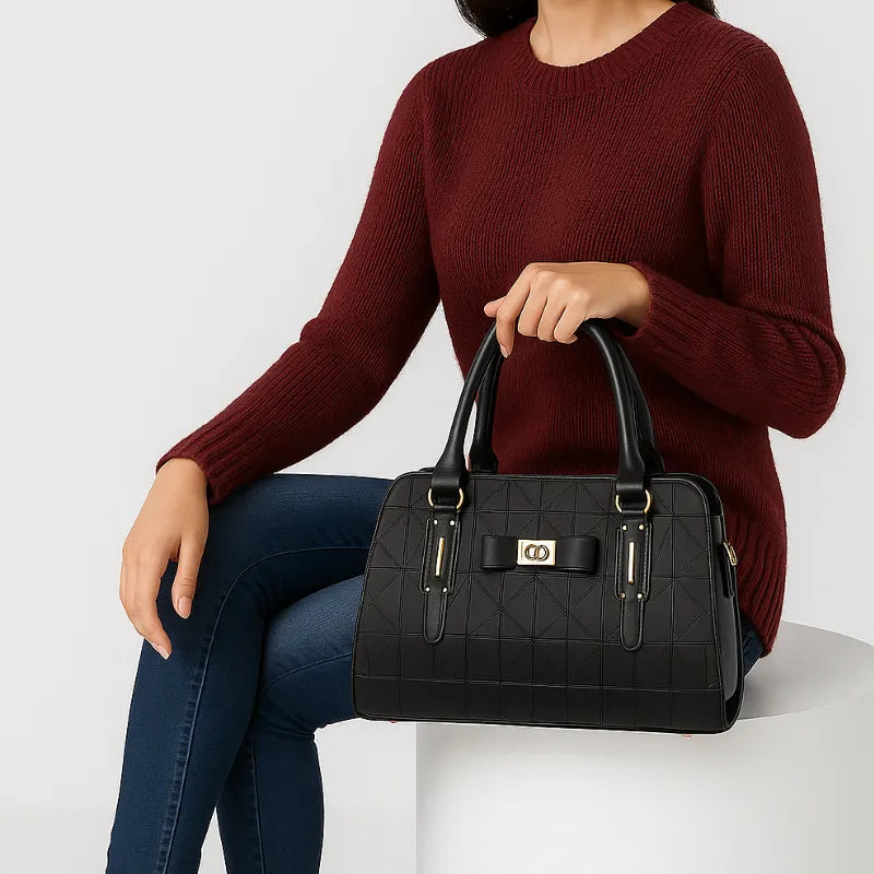 Modelo usando a bolsa de ombro preta Charme Clássico da Rozze, sentada. A imagem mostra o acessório em uso, com a alça de mão, ideal para looks de trabalho ou eventos.