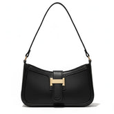 Bolsa de ombro feminina preta, vista frontal em estúdio. A foto destaca o formato baguette e o fecho de barra metálica dourada.