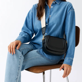 Modelo usando a bolsa de ombro Florence da Rozze, sentada. A imagem mostra o acessório em uso, com foco na alça removível e no fechamento por ferrolho.