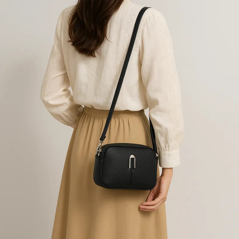 Bolsa preta transversal de couro sintético sendo usada por uma mulher em pé com pose elegante, mostrando versatilidade.