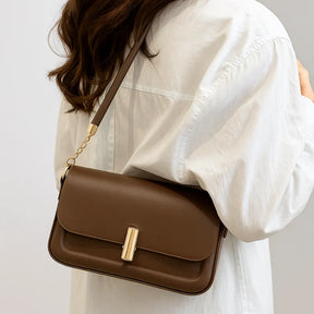 Modelo usando a bolsa retangular marrom no ombro. A imagem realça o estilo elegante e o tamanho compacto do acessório.