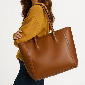 Modelo usando a bolsa tote caramelo. A imagem mostra o acessório sendo carregado no ombro, realçando seu tamanho grande e estilo elegante.