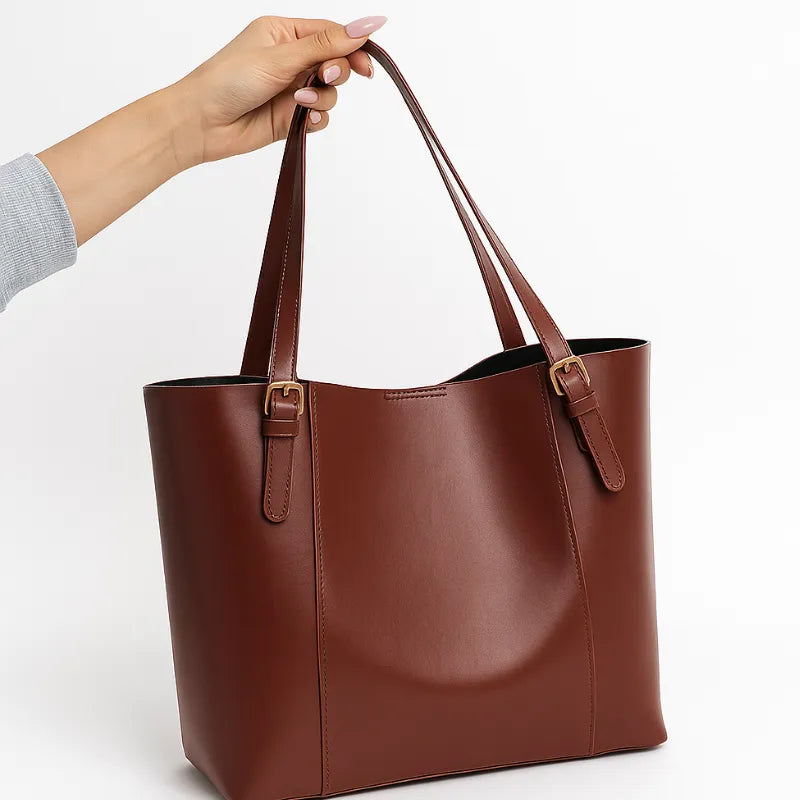 Modelo segurando a bolsa tote marrom pelas alças. A foto em close destaca o material em Couro PU e o design moderno.