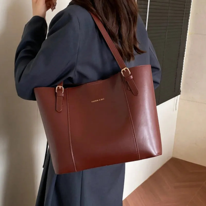 Modelo usando a bolsa tote marrom em vista lateral. A foto realça a praticidade da alça e o caimento da bolsa grande ao corpo.