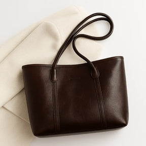 Vista superior da bolsa tote marrom escuro. A foto em close destaca o material e o detalhe das alças de punho duplo.