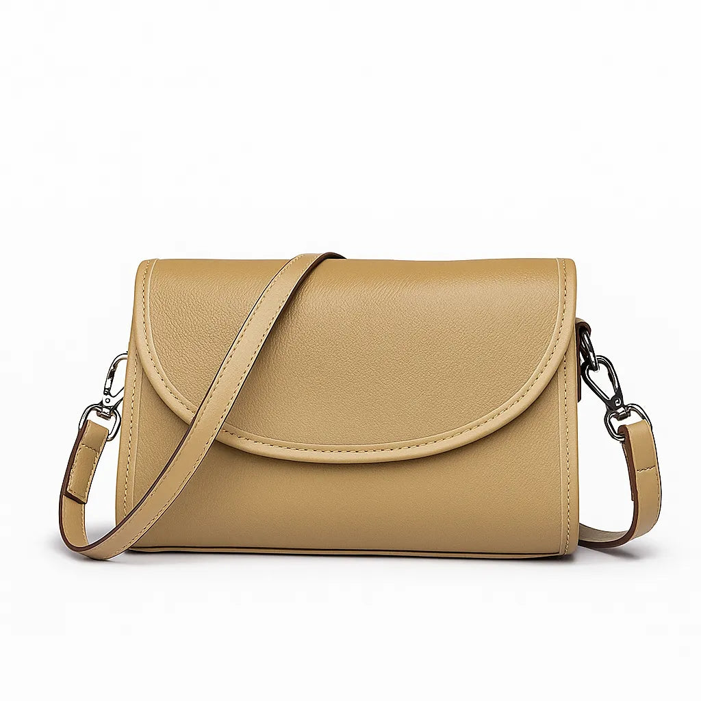 Bolsa transversal feminina bege de couro genuíno. Vista frontal em estúdio, destacando o design atemporal com aba arredondada, fechamento por zíper e alça ajustável.
