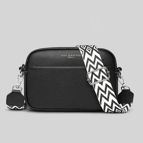 Bolsa transversal preta com alça listrada, vista frontal, destacando design moderno e couro genuíno