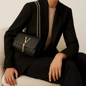 Bolsa Vogue preta com corrente sendo usada por uma mulher sentada com pose relaxada, mostrando sofisticação.
