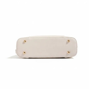 Vista inferior da bolsa de ombro bege. A foto detalha os pés de metal dourados que protegem a base da bolsa.