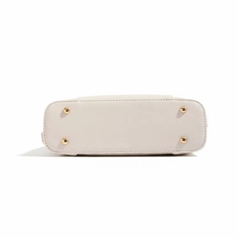 Vista inferior da bolsa de ombro bege. A foto detalha os pés de metal dourados que protegem a base da bolsa.