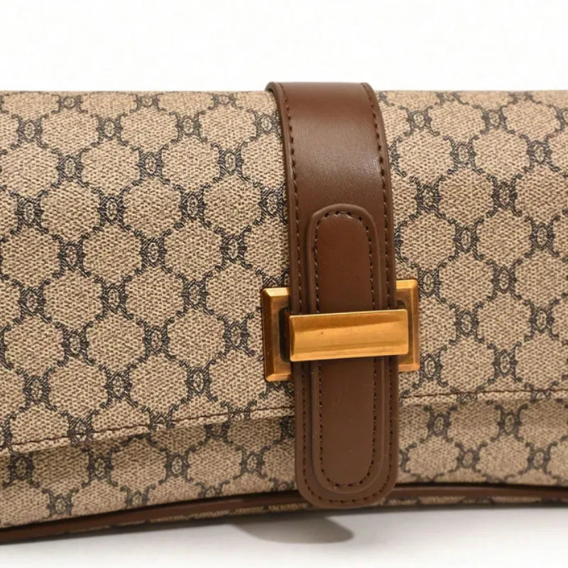 Detalhe da trava dourada e do canvas monograma. A foto em close aproxima o design sofisticado da aba de fecho.