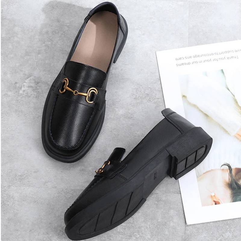 Par de loafers pretos femininos com fivela sobre fundo claro, destacando salto baixo e material PU.