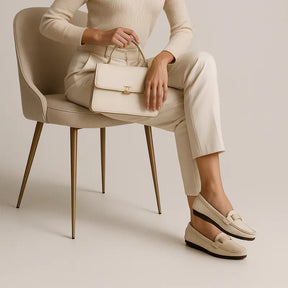 Modelo usando o mocassim branco de couro da Rozze, com as pernas cruzadas. A imagem enfatiza o estilo clássico e a versatilidade do acessório.