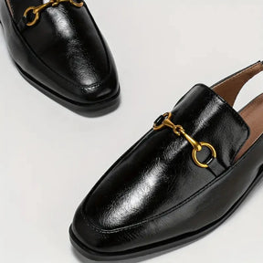 Detalhe da sapatilha preta slingback da Rozze, em vista de ângulo. A foto aproxima o material com acabamento em brilho e o detalhe metálico dourado na parte superior.