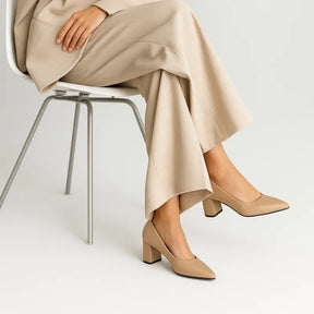 Scarpin salto bloco beige bico fino sendo usado por uma mulher sentada com pose relaxada, exibindo conforto.
