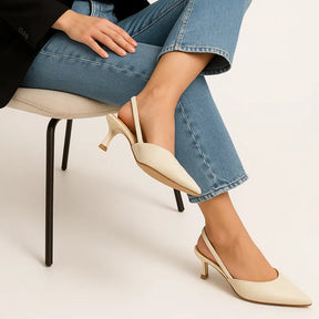 Modelo usando o scarpin marfim slingback da Rozze, em pé. A foto de perfil enfatiza a elegância do salto agulha e a forma do sapato no pé.