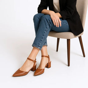 Modelo usando o scarpin marrom com salto bloco da Rozze, sentada. A imagem mostra o calçado em uso, complementando um look casual elegante com calça jeans.