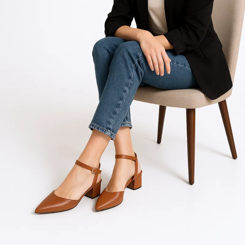 Modelo usando o scarpin marrom com salto bloco da Rozze, sentada. A imagem mostra o calçado em uso, complementando um look casual elegante com calça jeans.