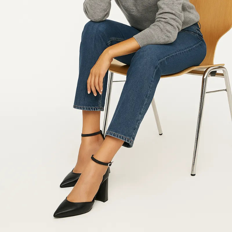 Modelo usando o scarpin preto com tira no tornozelo da Rozze, sentada. A imagem mostra o calçado em uso, complementando um look casual elegante com calça jeans e blazer.