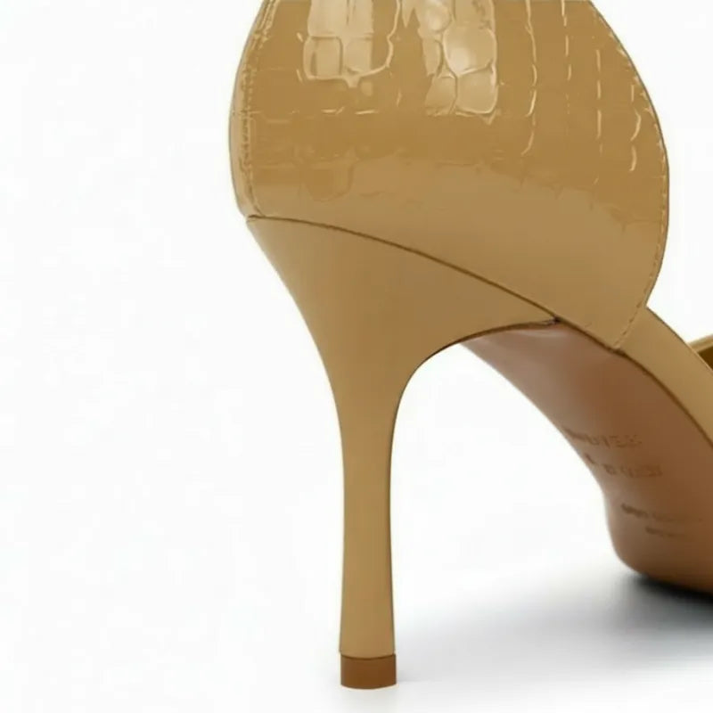 Detalhe do salto alto fino e do acabamento em verniz nude. A foto em close destaca a textura crocodilo sofisticada no calcanhar.