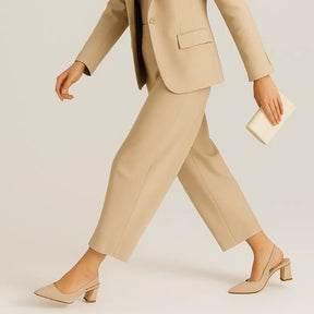 Modelo usando o scarpin slingback em camurça, em pé. A foto de perfil enfatiza o design atemporal do sapato e a estabilidade do salto bloco.