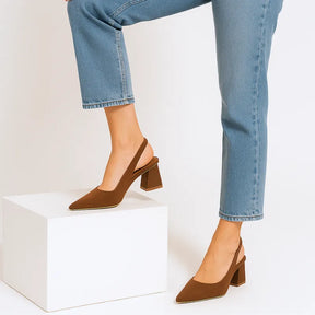 Modelo em pé com o scarpin slingback marrom da Rozze sobre um bloco. A imagem realça a versatilidade do calçado e a sua combinação com diferentes estilos.