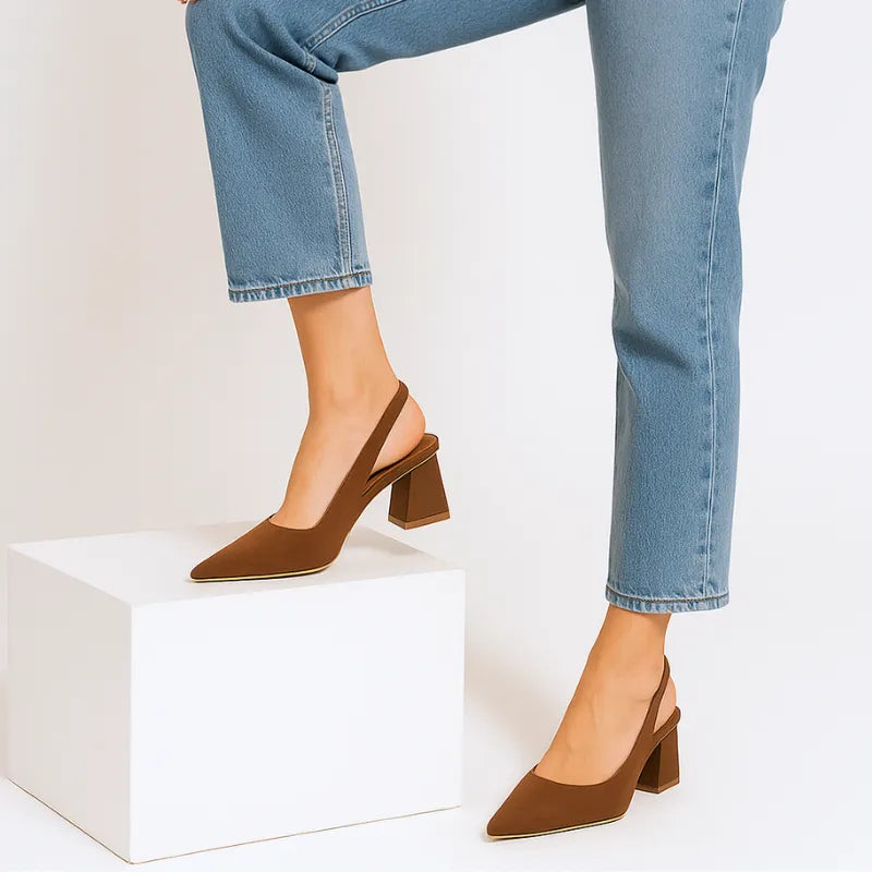Modelo em pé com o scarpin slingback marrom da Rozze sobre um bloco. A imagem realça a versatilidade do calçado e a sua combinação com diferentes estilos.