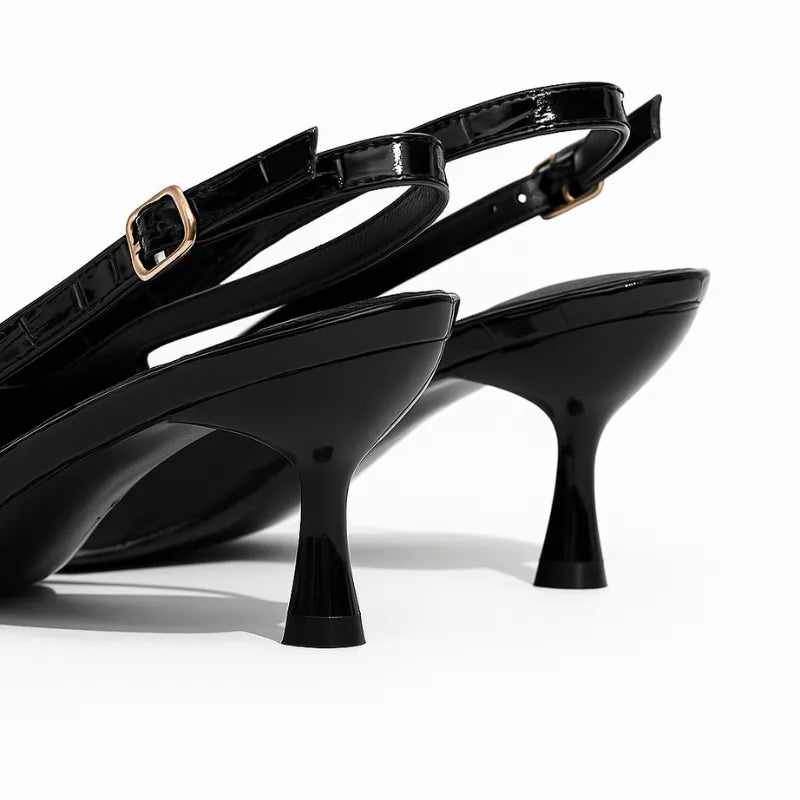 Detalhe do salto e da alça traseira do scarpin preto. A foto em close mostra o formato do salto, a fivela dourada e o material em couro PU.